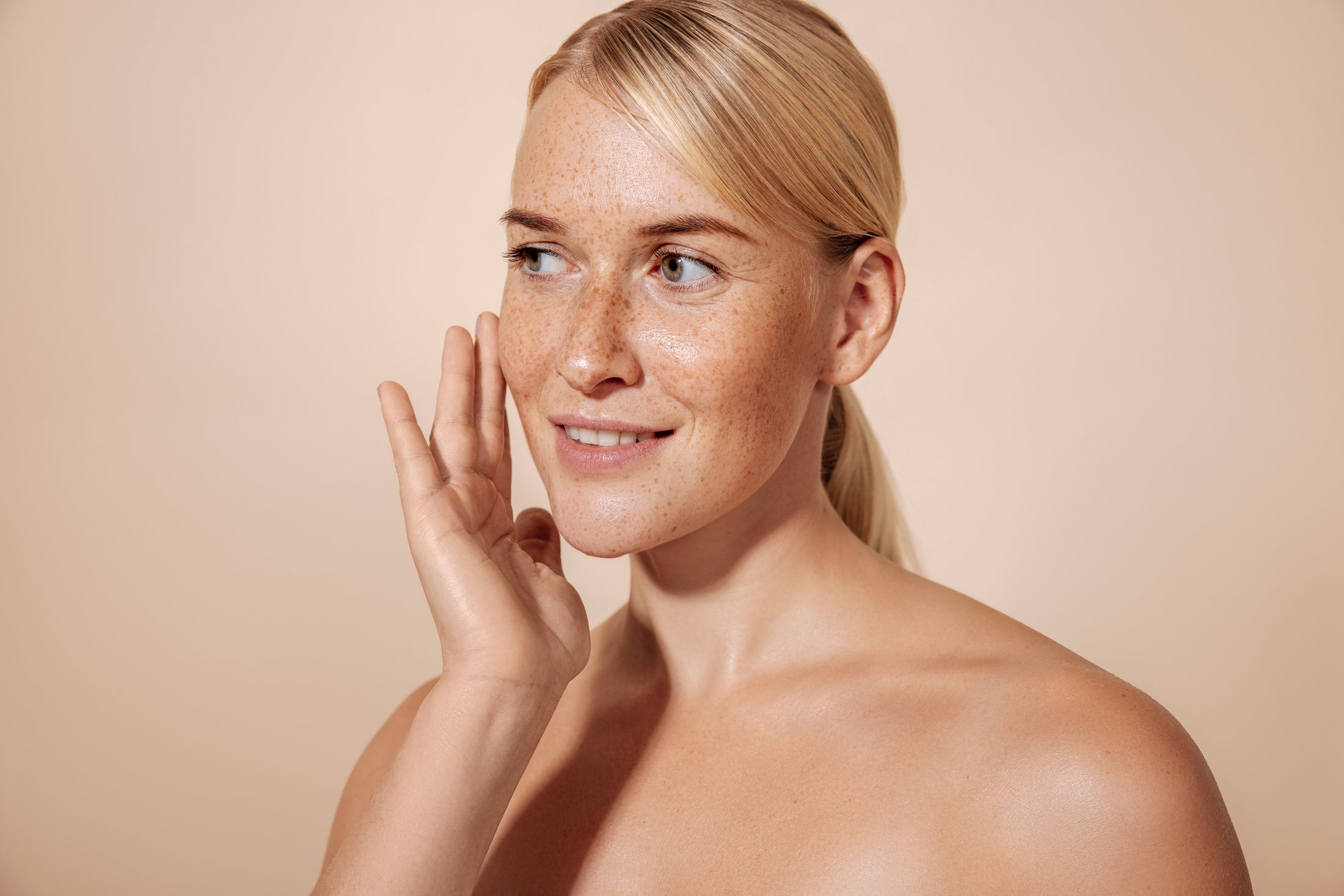 Smiling woman with freckles on neutral background.